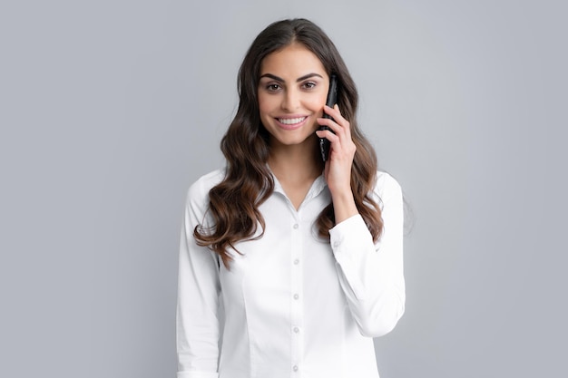 Mulher feliz falando no telefone Jovem empresária morena sorridente na camisa segura smartphone isolado no retrato de estúdio de fundo cinza Menina de beleza usando telefone celular