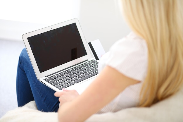 Mulher feliz fazendo compras online em casa. close-up de uma mão segurando um cartão de crédito ao lado de um laptop.