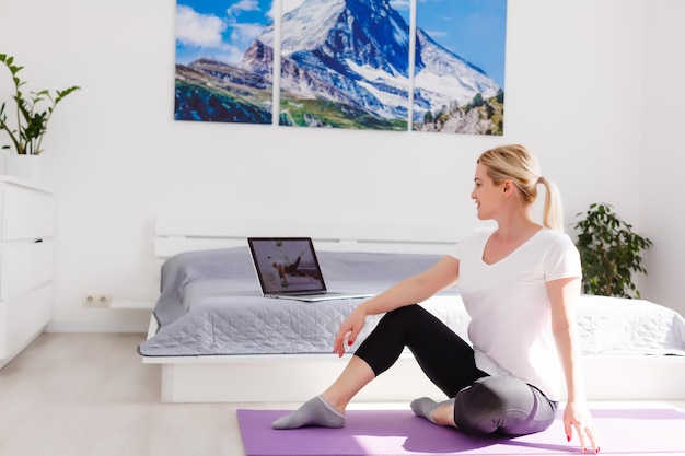 Mulher feliz fazendo exercícios enquanto assiste a um vídeo de treino no laptop em casa