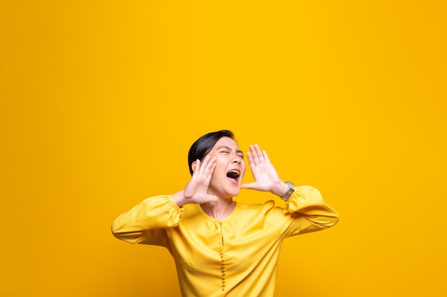 Mulher feliz fazendo grito gesto isolado sobre parede amarela