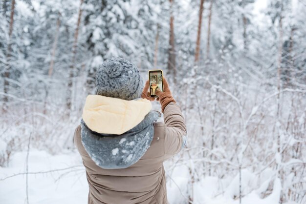 Mulher feliz fazendo selfie com smartphone na bela floresta de inverno nevado
