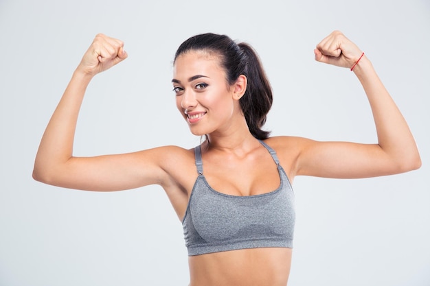 Mulher feliz fitness mostrando seu bíceps isolado em uma parede branca e olhando para a frente