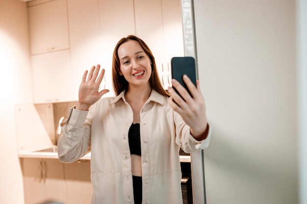 Mulher feliz freelancer em roupas casuais fazendo videochamada para amigos em pé na cozinha de casa durante o freio de trabalho Oi, prazer em conhecê-lo