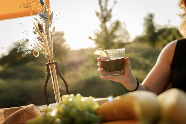 Mulher feliz freelancer usa telefone e bebe uma chamada de coquetel enquanto relaxa na aconchegante barraca glamping em dia ensolarado Barraca de acampamento de luxo para férias de verão ao ar livre e férias Conceito de estilo de vida