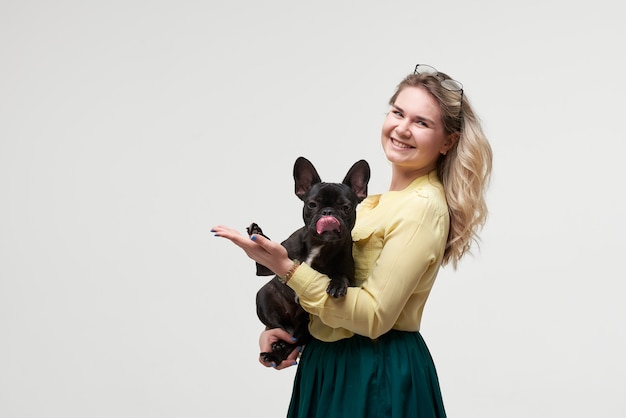 Mulher feliz hipster brincando com bulldog francês na parede branca