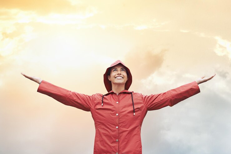 Foto mulher feliz impermeável e liberdade com tempo para céu nublado sol ou estação de inverno em tempestade ao ar livre pessoa feminina com sorriso em casaco de chuva à prova de água vermelho para nevoeiro nublado ou neve em espaço de maquete