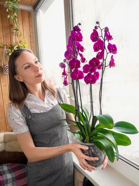 Mulher feliz jardineira com uma orquídea florescendo em uma panela Pote de phalaenopsis de planta de orquídea florida nas mãos Criação de orquídeas na primavera Floricultura em casa