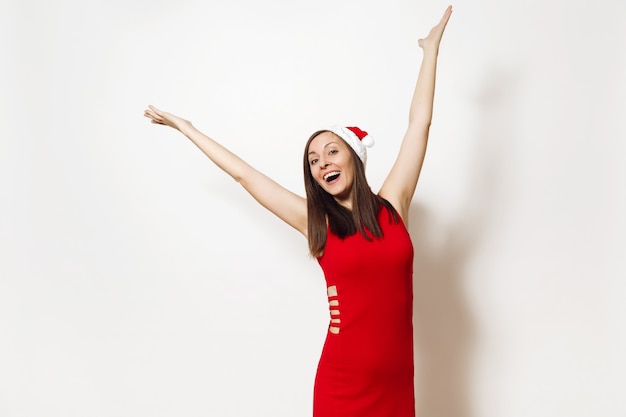 Mulher feliz jovem bonita caucasiana com sorriso encantador usando vestido vermelho e chapéu de Natal, espalhando as mãos isoladas no fundo branco. Menina Santa. Feriado de ano novo de 2018. Copie o espaço para anúncio