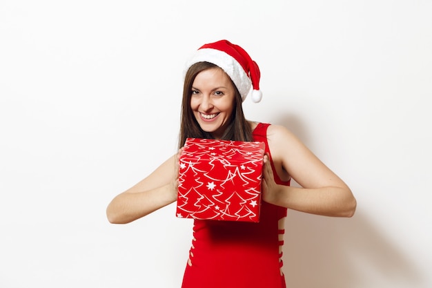 Mulher feliz jovem caucasiana bonita com sorriso encantador vestida com um vestido vermelho e chapéu de Natal segurando uma caixa de presente em fundo branco. Menina santa com presente isolado. Conceito de feriado de ano novo 2018