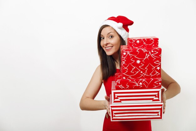 Mulher feliz jovem caucasiana bonita com um sorriso encantador vestida com um vestido vermelho e chapéu de Natal segurando caixas de presente em fundo branco. Menina santa com presente isolado. Conceito de feriado de ano novo 2018