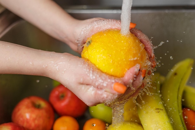 Mulher feliz lavando frutas na cozinha bananas tangerinas maçãs