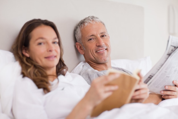 Mulher feliz lendo um livro enquanto o marido está lendo as notícias