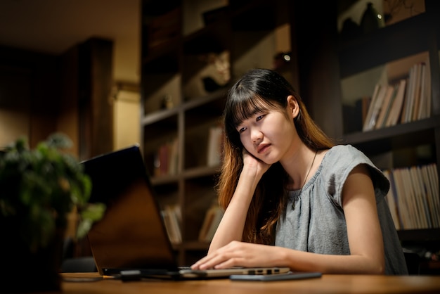 Mulher feliz linda estudante asiática trabalhando no laptop na sala de biblioteca moderna