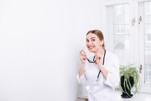 Mulher feliz, médica, com um jaleco branco e um estetoscópio no fundo da janela