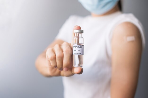 Mulher feliz mostrando o frasco da vacina COVID-19 e o braço com curativo após receber a vacinação. imunização, inoculação e pandemia de Coronavírus