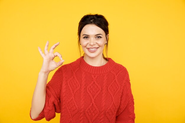 Mulher feliz mostrando ok isolado na parede amarela brilhante.