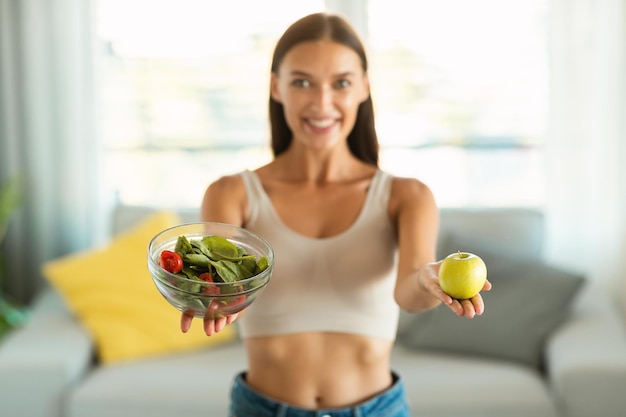 Mulher feliz mostrando salada e maçã recomendando dieta em casa