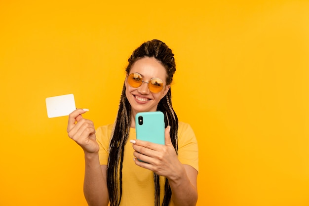 Mulher feliz na camiseta amarela segurando o cartão de crédito com o celular.