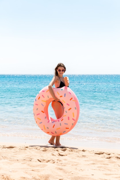 Mulher feliz na praia brincando com um anel de donut inflável. Férias de verão e o conceito de férias.