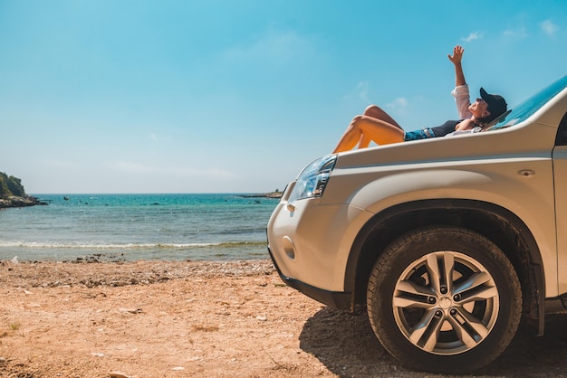 Mulher feliz na praia de verão do mar sentado no capô do carro