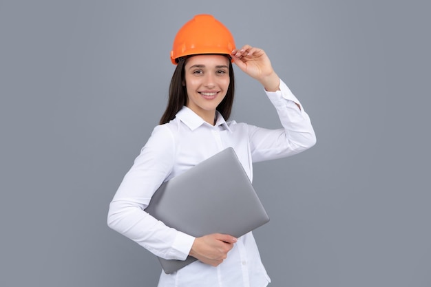Mulher feliz no capacete protetor de capacete com computador portátil isolado em fundo cinza Arquiteto