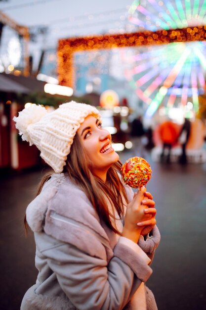 Mulher feliz no mercado de Natal com maçã caramelizada Atividades ao ar livre no Natal