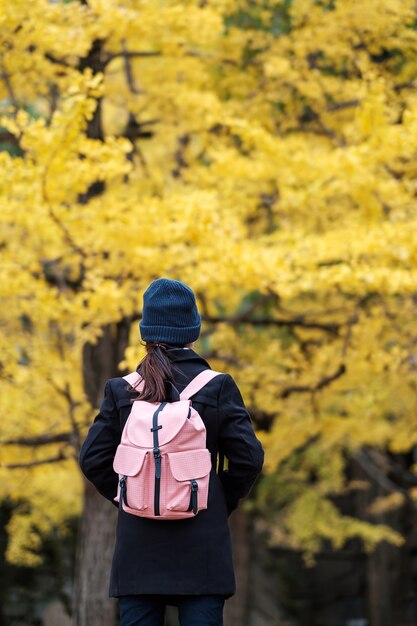 Mulher feliz no parque ao ar livre na temporada de outono. Viajante asiático com casaco e chapéu contra o fundo de folhas amarelas de Ginkgo