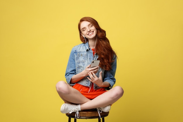 Mulher feliz nos fones de ouvido que escuta a música e que canta ao sentar e ao guardar o telefone celular.