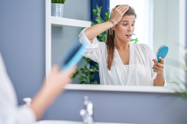 Mulher feliz penteando o cabelo no banheiro e tendo problemas com queda de cabelo