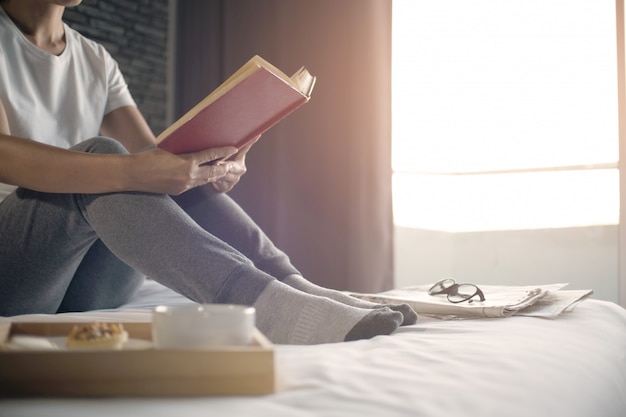 Mulher feliz que lê um livro e que relaxa confortavelmente em casa.