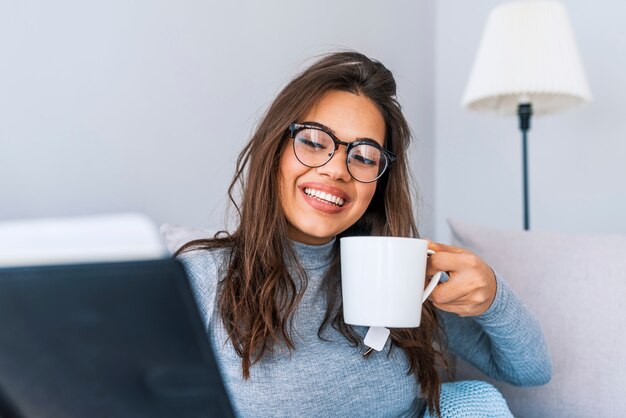 Mulher feliz que relaxa em casa no inverno acolhedor ou no fim de semana do outono com livro e copo do chá quente