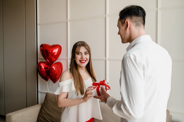 Mulher feliz recebe presente de homem com coração vermelho em forma de balões em casa