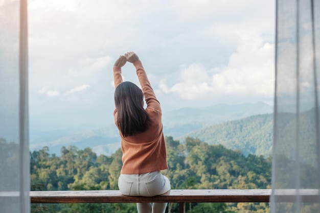 Mulher feliz relaxando e olhando para a vista da montanha em casa de campo ou homestay pela manhã Viagem de viagem de blogueiro de férias SoloTravel e conceito relaxante