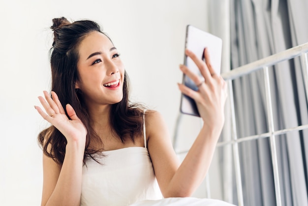 Mulher feliz relaxante usando computador tablet na cama em casa. conceito de tecnologia e comunicação