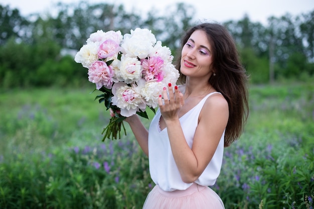 mulher feliz segurando buquê de peônias linda garota com peônias apreciando flores no fundo da natureza