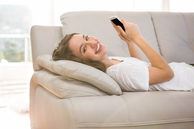 Mulher feliz, segurando o telefone enquanto estabelece no sofá