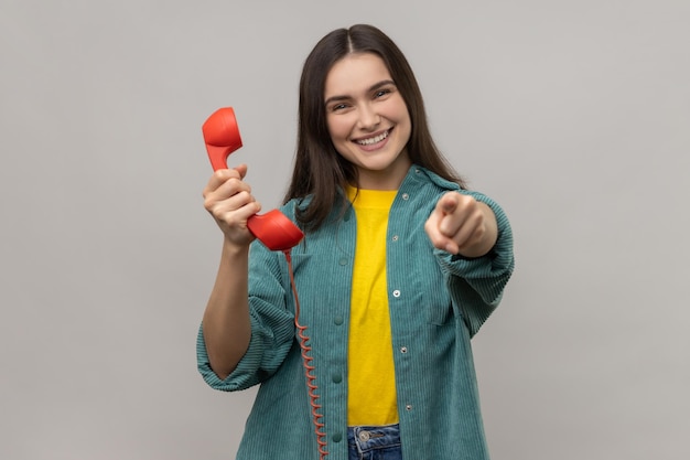 Mulher feliz segurando o telefone fixo vermelho e apontando para a câmera com o dedo me ligue estou esperando