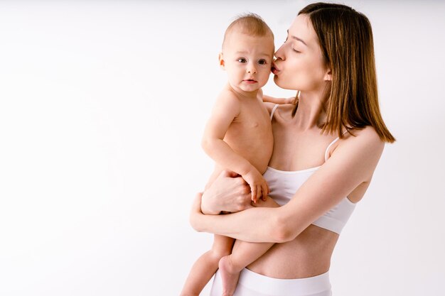 Mulher feliz segurando seu bebê em fundo colorido - jovem mulher vestindo cueca cuidando de seu filho pequeno - gravidez, maternidade, pessoas e conceito de expectativa