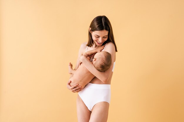 Mulher feliz segurando seu bebê em fundo colorido - Jovem mulher vestindo cueca cuidando de seu filho pequeno - Gravidez, maternidade, pessoas e conceito de expectativa