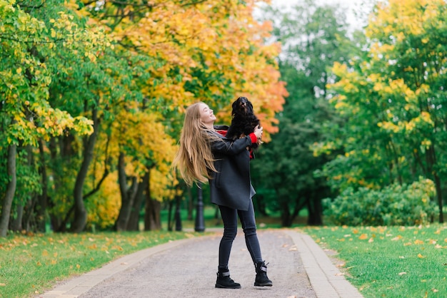 Mulher feliz segurando seu cachorrinho nos braços, parque outono