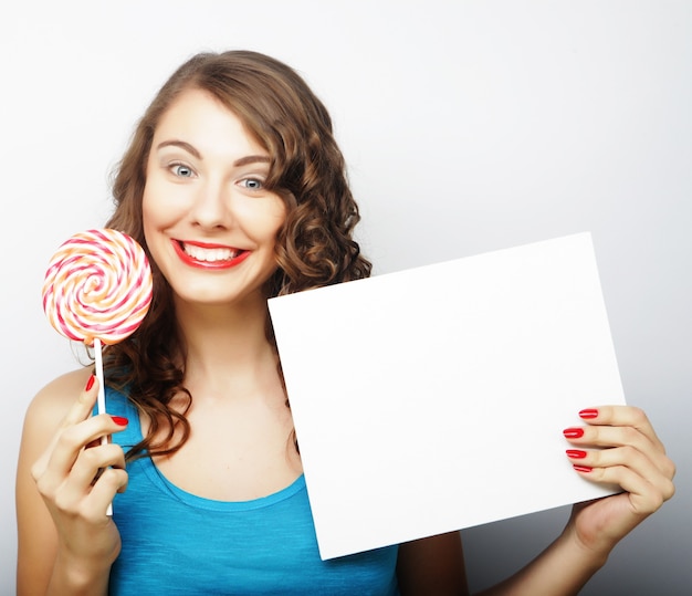 Foto mulher feliz segurando um cartão em branco e pirulito. sobre fundo branco, sorrindo retrato feminino.