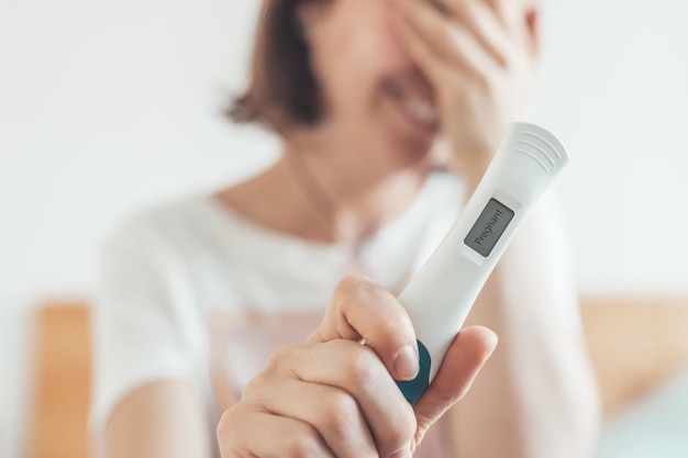 Mulher feliz sentada na cama verificando teste de gravidez Resultado positivo Grávida