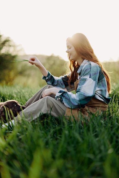 Mulher feliz sentada na natureza e brincando com seu animal de estimação no parque sentada na grama verde na luz do sol de verão à noite brincando na natureza foto de alta qualidade