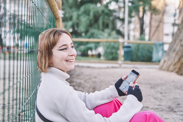 Mulher feliz sentada na rua com o celular na mão