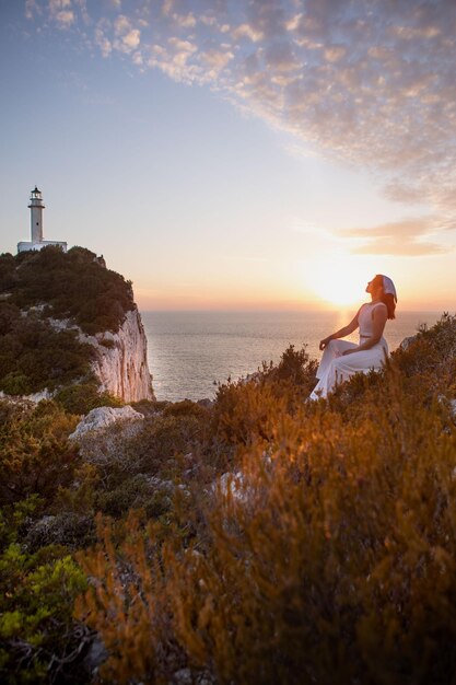 Mulher feliz sentada na vista do penhasco do farol da ilha de Lefkada