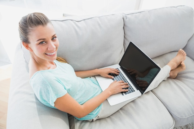 Mulher feliz sentada no sofá usando o laptop sorrindo para a câmera