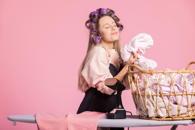 Mulher feliz sorridente em fundo rosa cheira roupa limpa e lavada com cheiro de frescor em pó