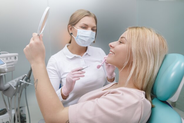 Mulher feliz sorrindo olhando no espelho após exame dentário