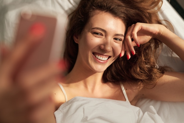 Foto mulher feliz tirando uma selfie na cama de manhã