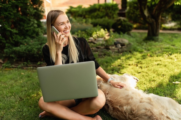 Foto mulher feliz trabalhando com laptop e brincando com o cachorro labrador no parque verde